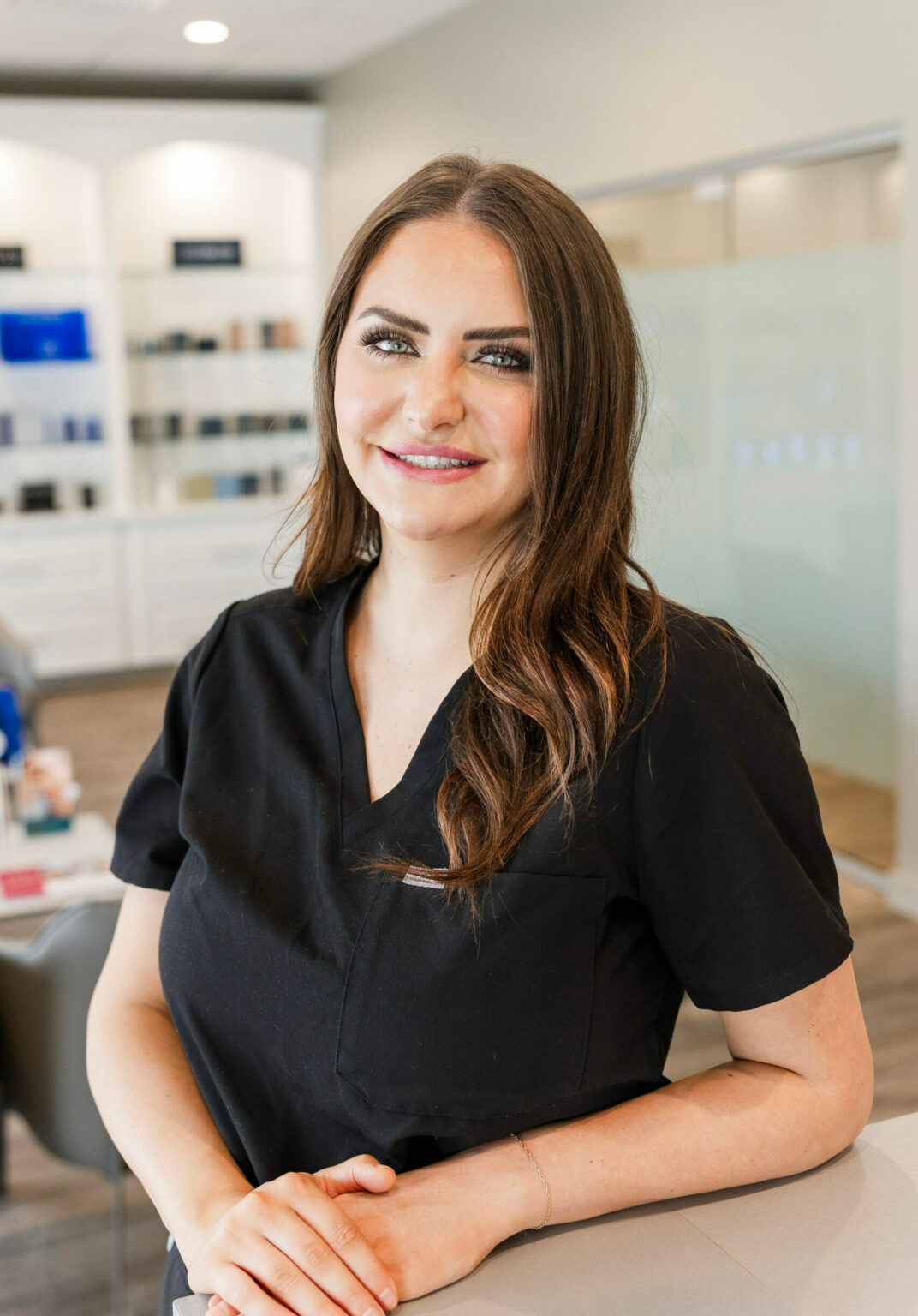 Woman in black scrubs, smiling, leaning on a counter, professional setting.