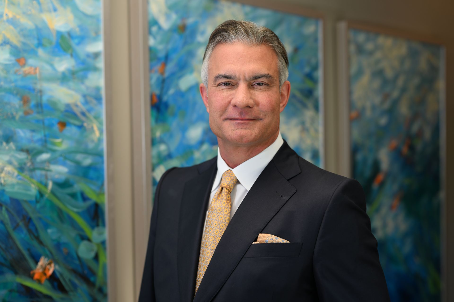 Man in suit and tie posing in front of abstract blue artwork.