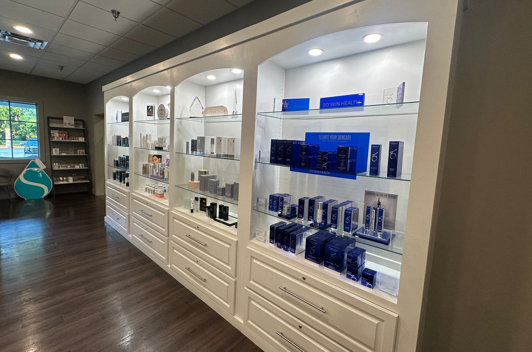 Display case in store with beauty products, wooden floor, white cabinets, and lighting.