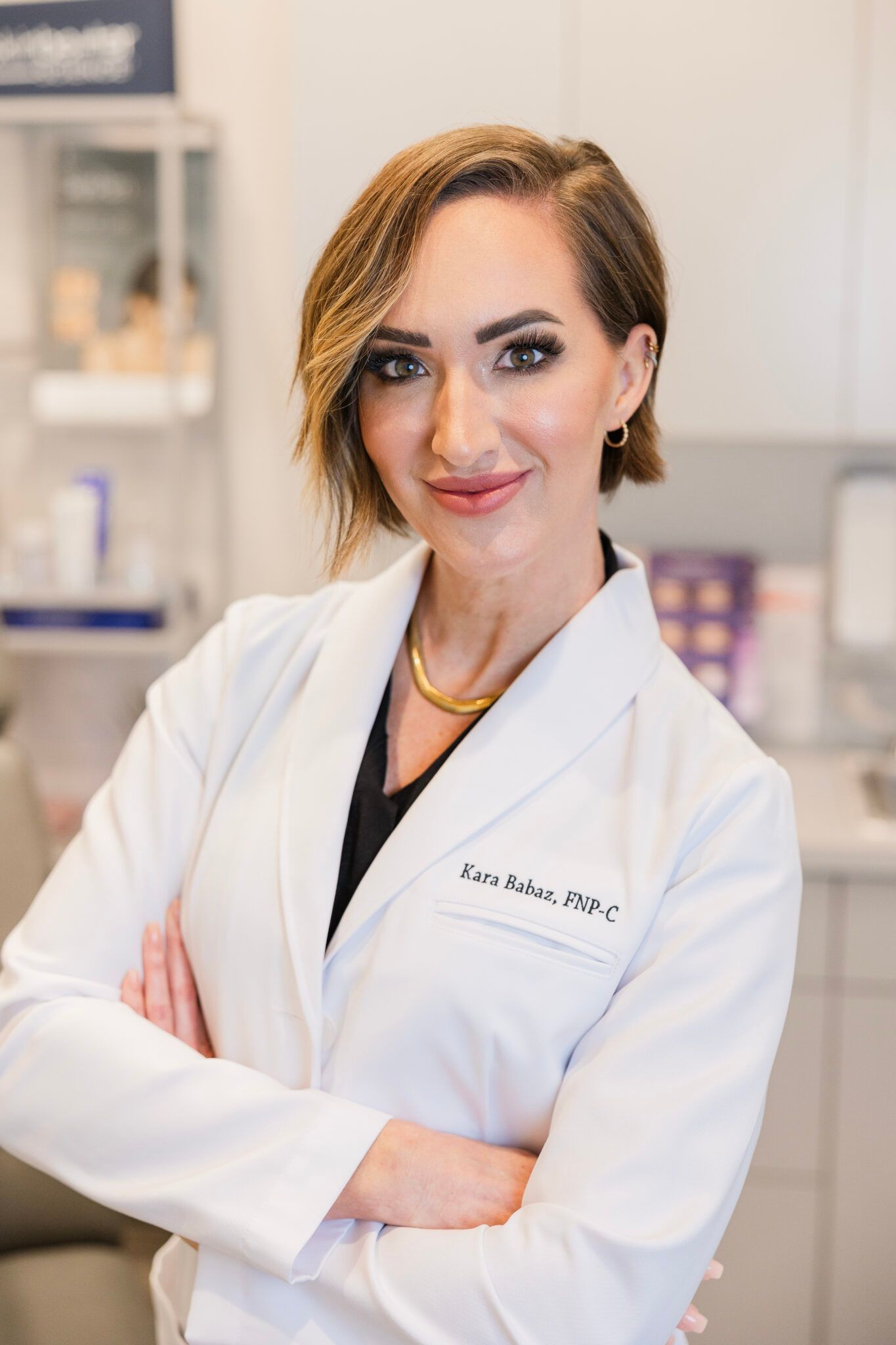 Woman in white lab coat with arms crossed, smiling in a medical setting.
