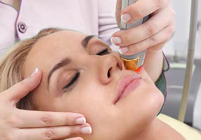 Woman receiving laser skin treatment on her nose; close-up shows device and technician’s hand.