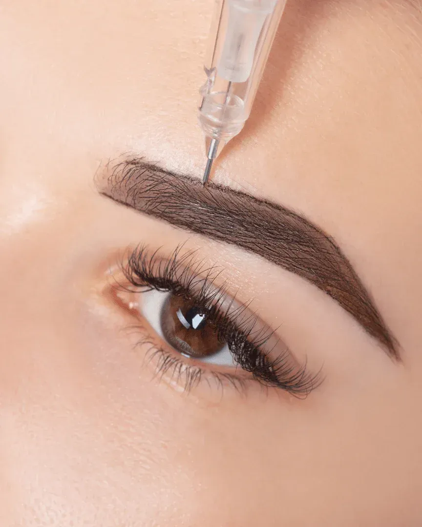 Eyebrow being tattooed with a needle. Close up of eye and eyebrow; needle is visible.