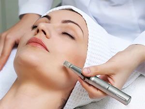 Woman receiving micro-needling treatment on her cheek; close-up, spa setting.