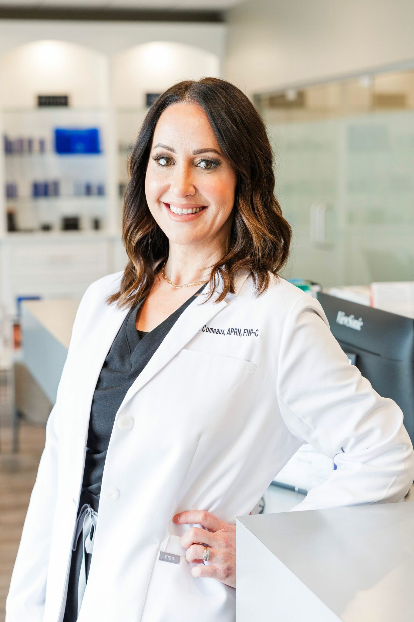 Woman in a white lab coat smiles, leaning on a counter, professional setting.