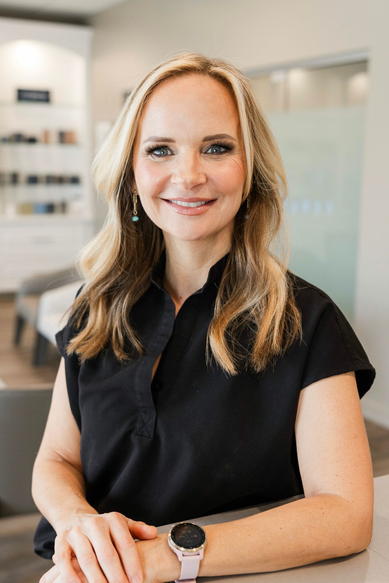 Woman with blonde hair wearing black shirt, smiling indoors.