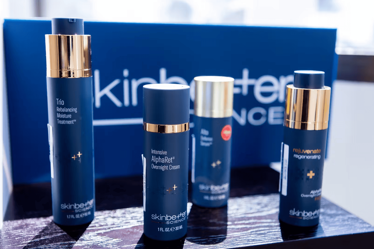 Cosmetic skincare products in navy blue bottles with gold caps, on a dark display stand.