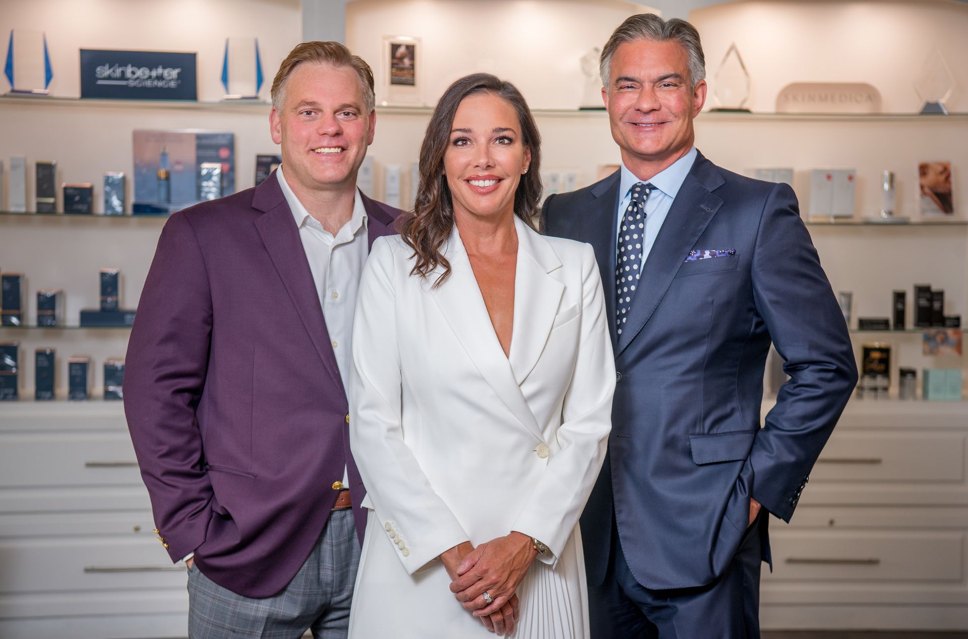 Four people in suits stand in front of a textured wall with a green logo, smiling.