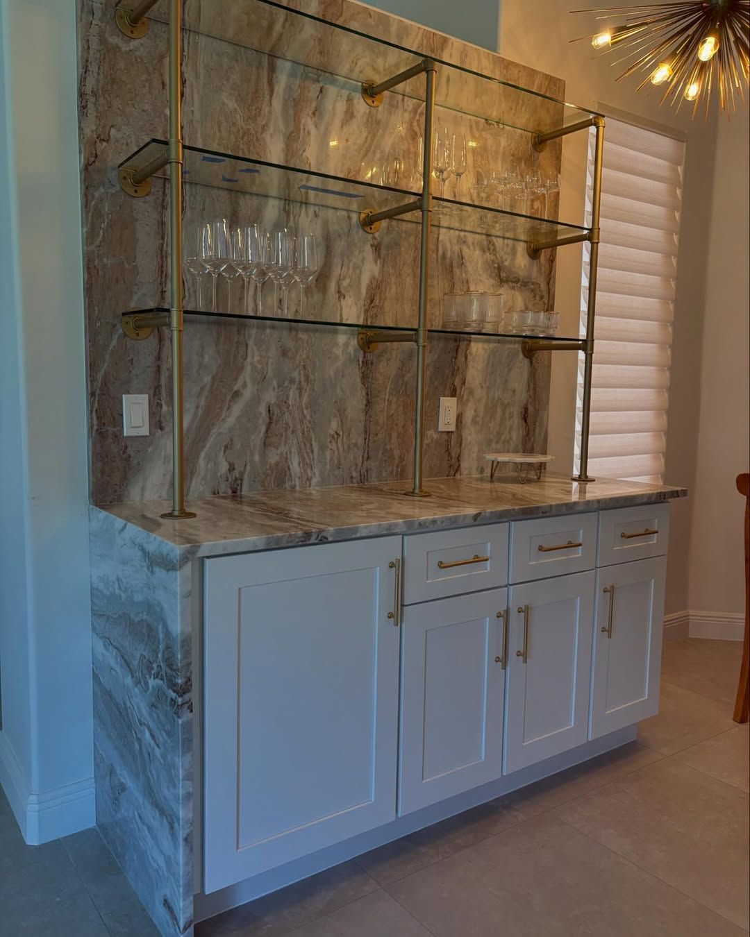 Built-in white cabinet with glass shelving and brass frame displaying decor in a bright room