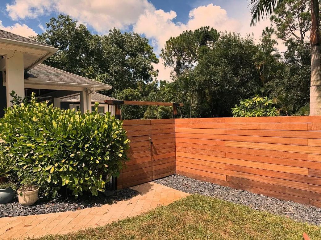 Backyard with a wooden privacy fence, gravel border, and leafy shrubs beside a house