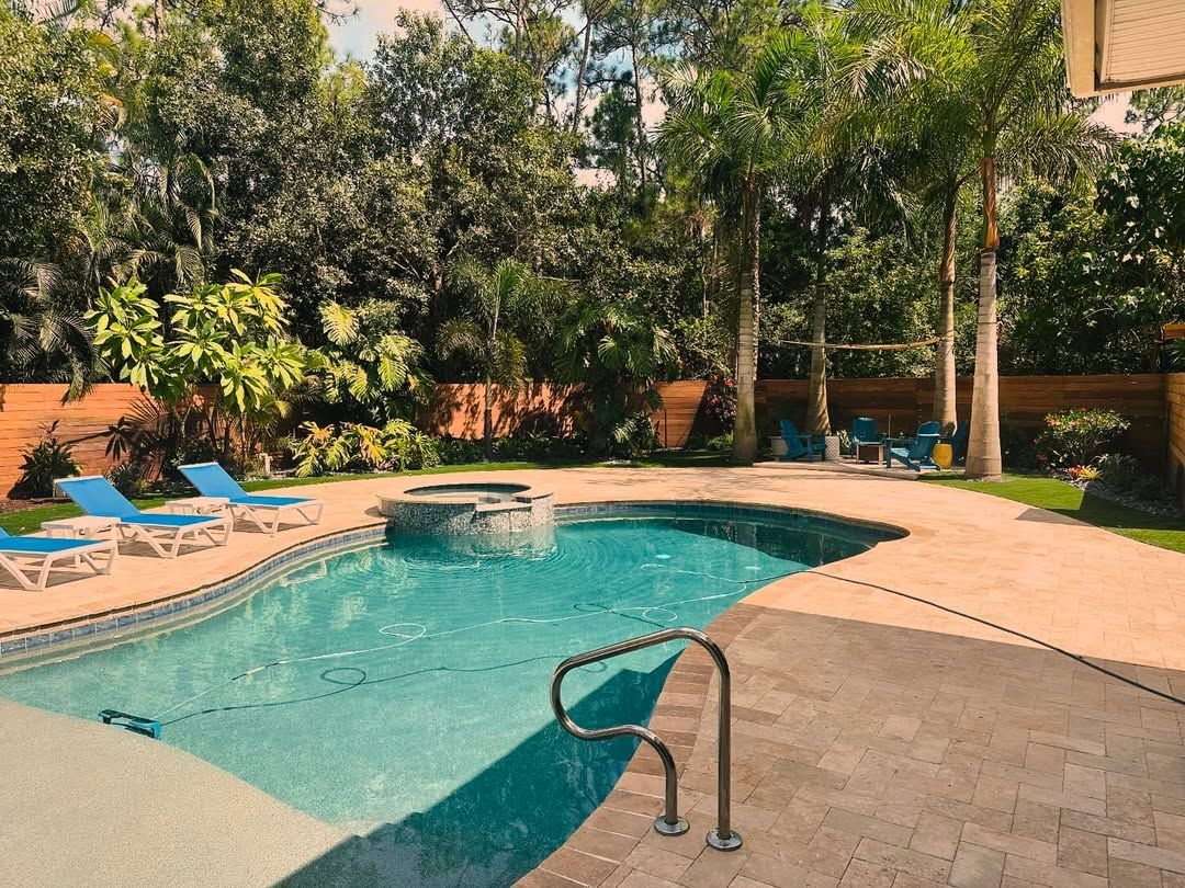 Backyard swimming pool with lounge chairs, trees, and a stone patio in bright sunlight