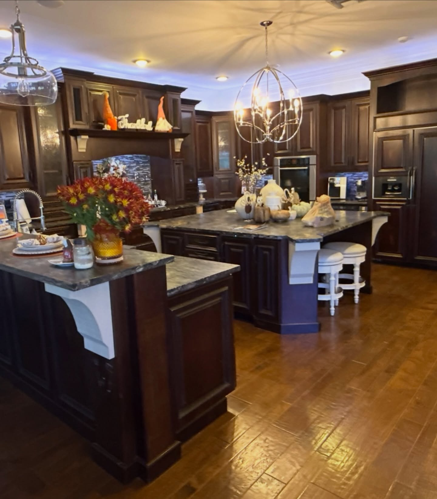 Dark wood kitchen with granite island, pendant lights, hardwood floors, and floral centerpiece