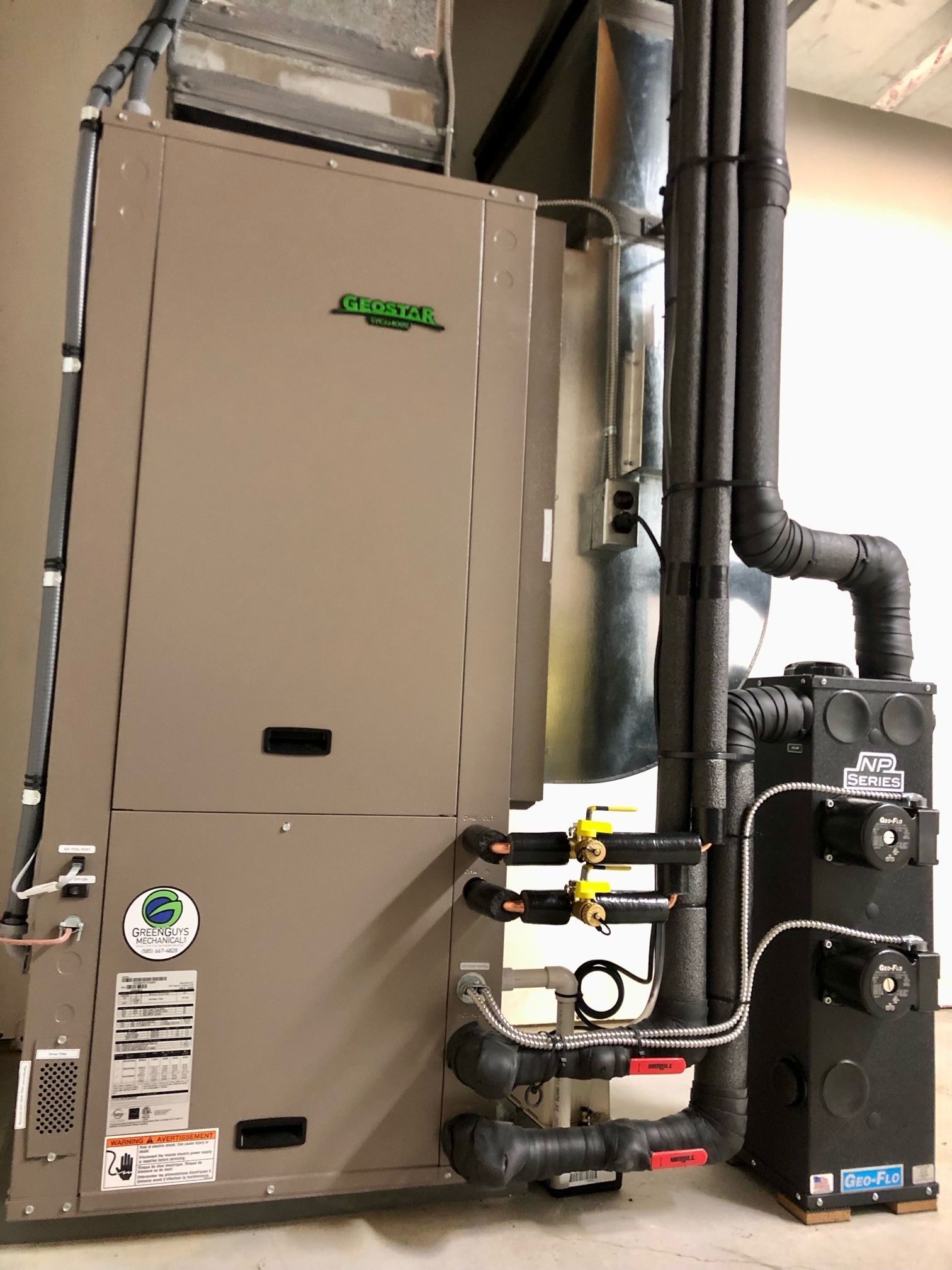 A beige heating and cooling unit with black pipes in a residential setting.