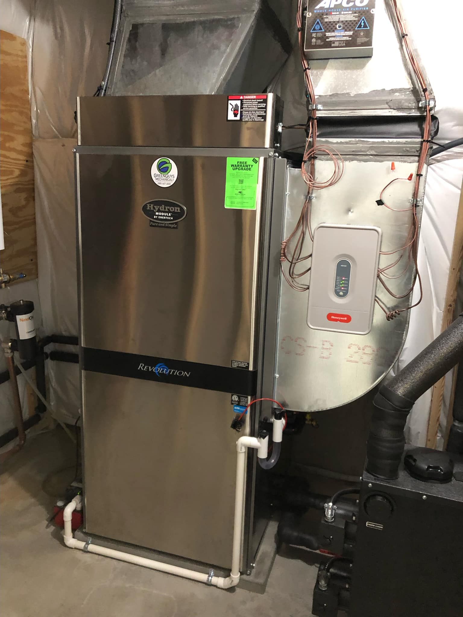 A large, stainless steel water heater next to a furnace in a basement.