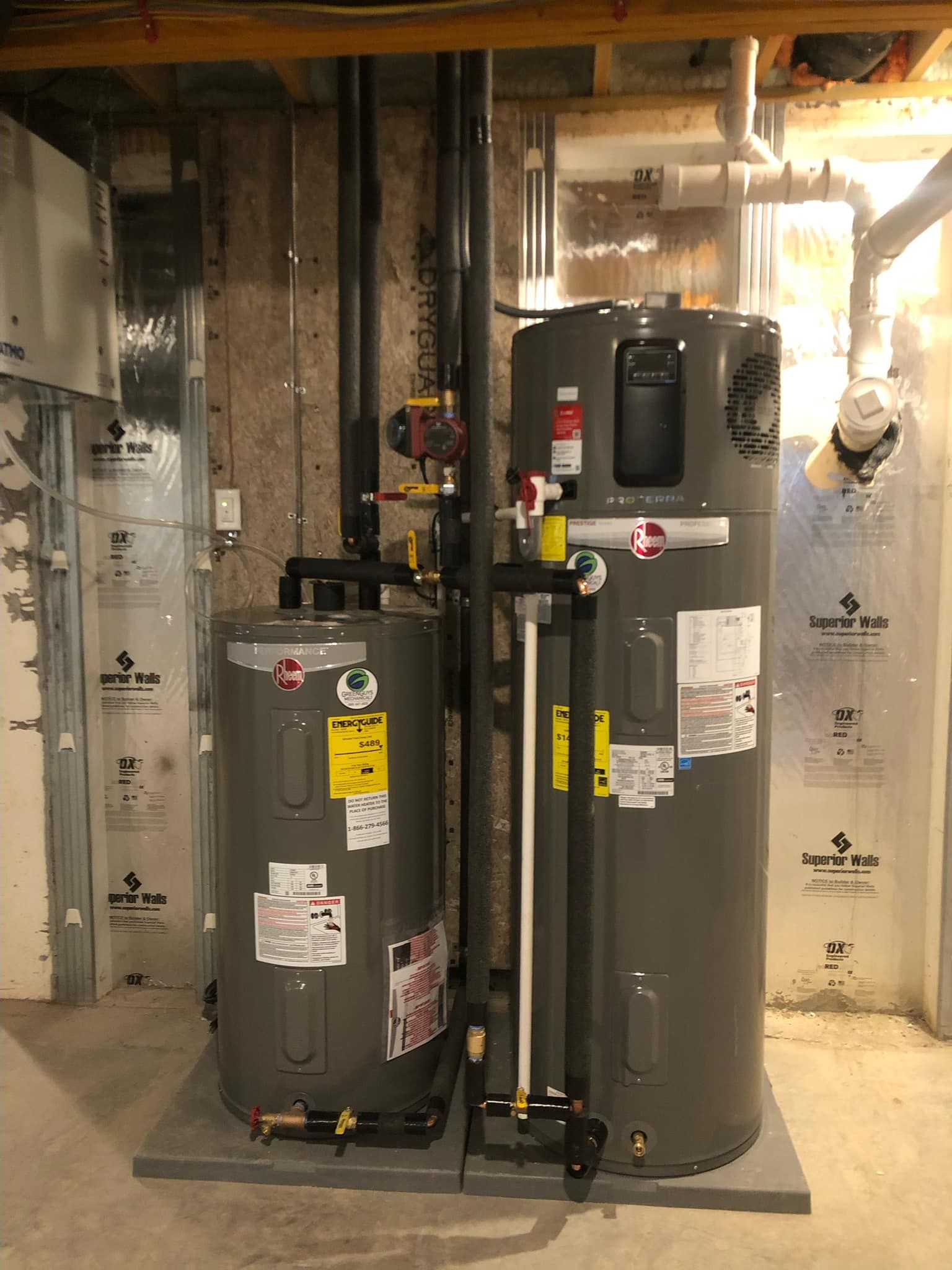 Two gray water heaters in a utility room, with pipes and insulation visible.