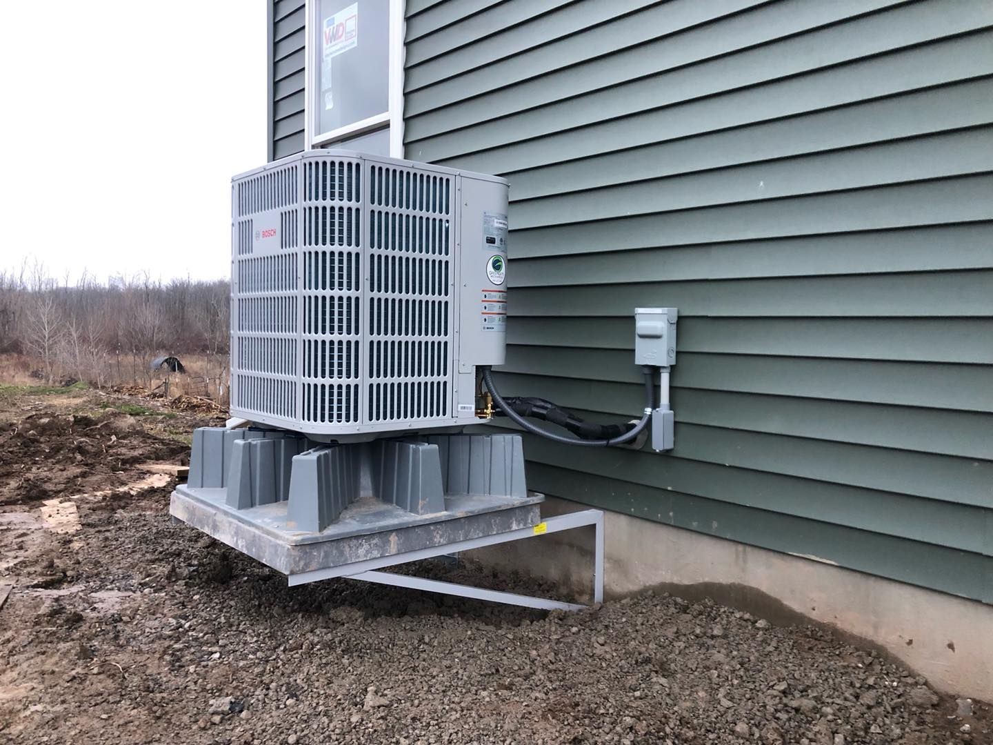 Air conditioning unit mounted on a grey platform next to a green house wall.