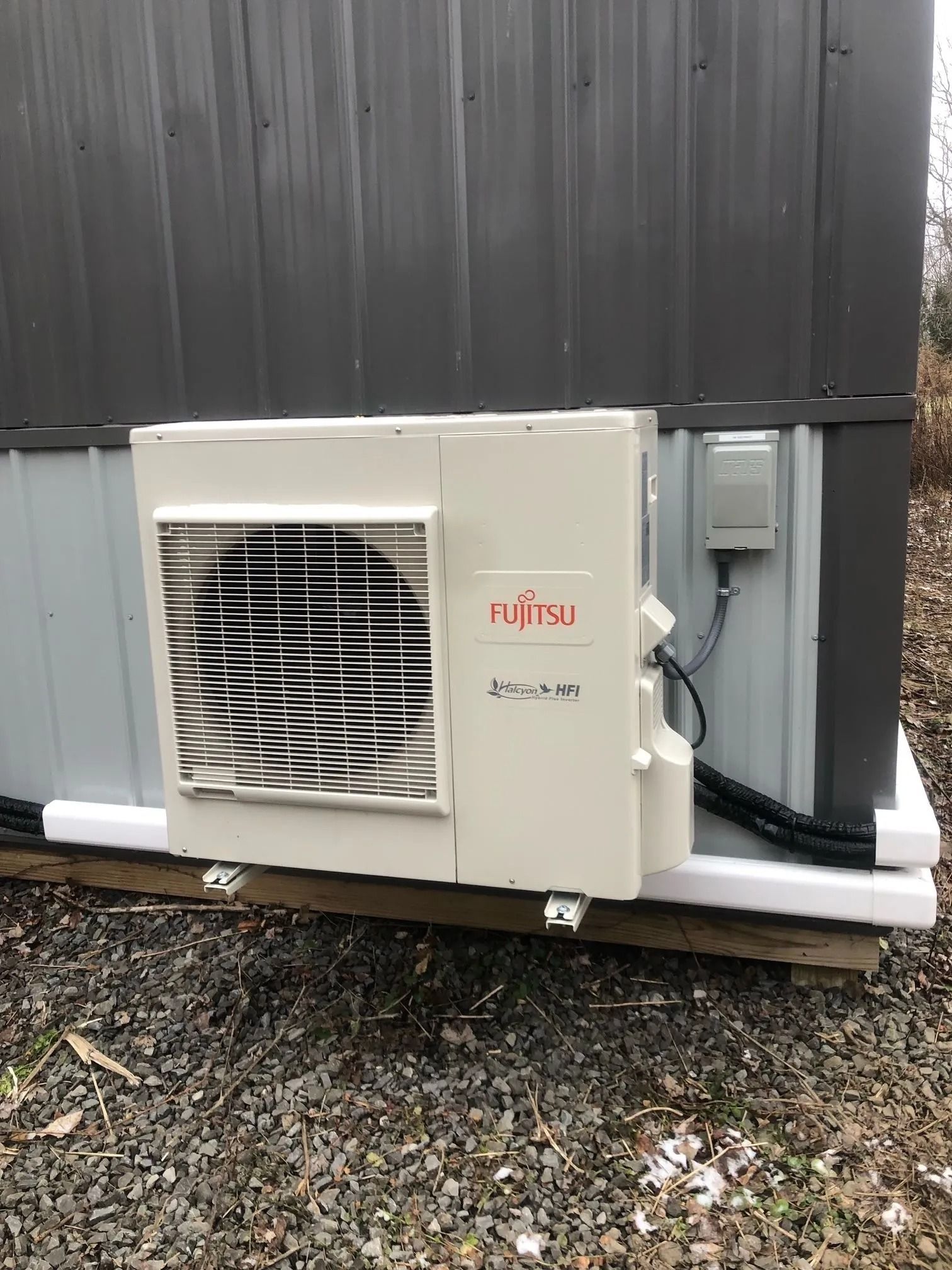 Fujitsu air conditioning unit mounted on a gray metal building, connected to electrical box.