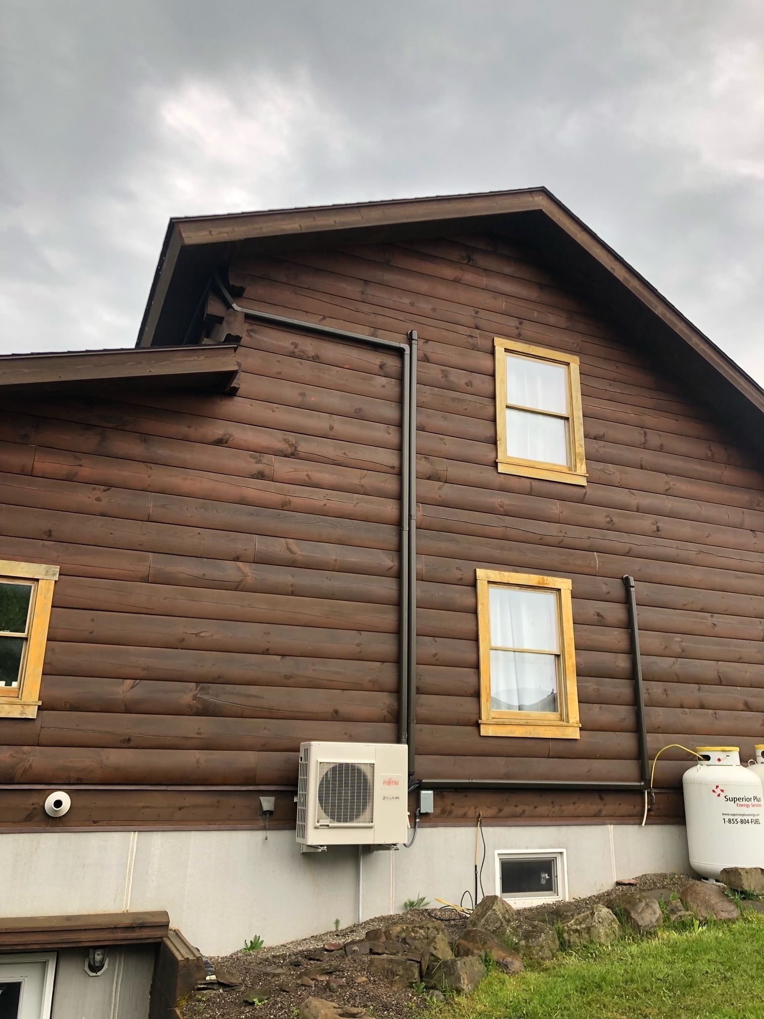Brown log cabin exterior with tan window frames, dark gutters, and an AC unit.