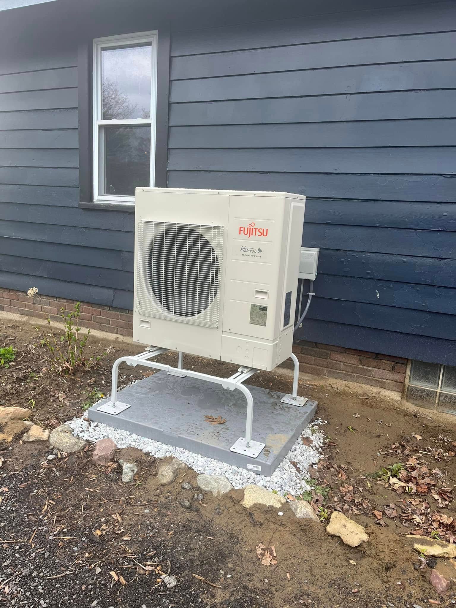 Exterior air conditioning unit mounted on a concrete pad near a building with dark blue siding and a window.