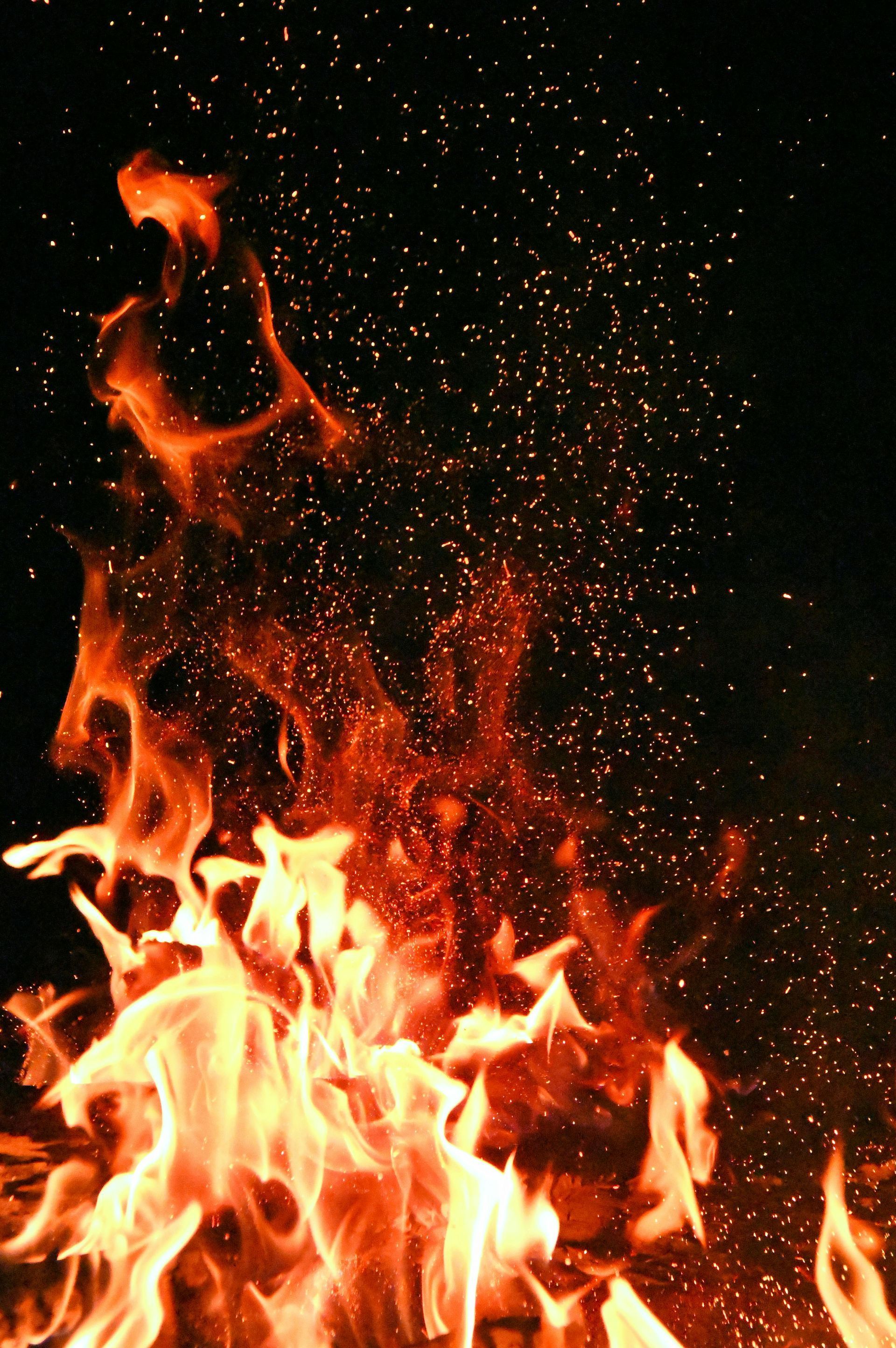 Flames burning intensely, orange and red against a dark background, with sparks rising.