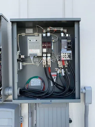 Electrical panel with wires and breakers inside a gray metal box mounted on a wall.