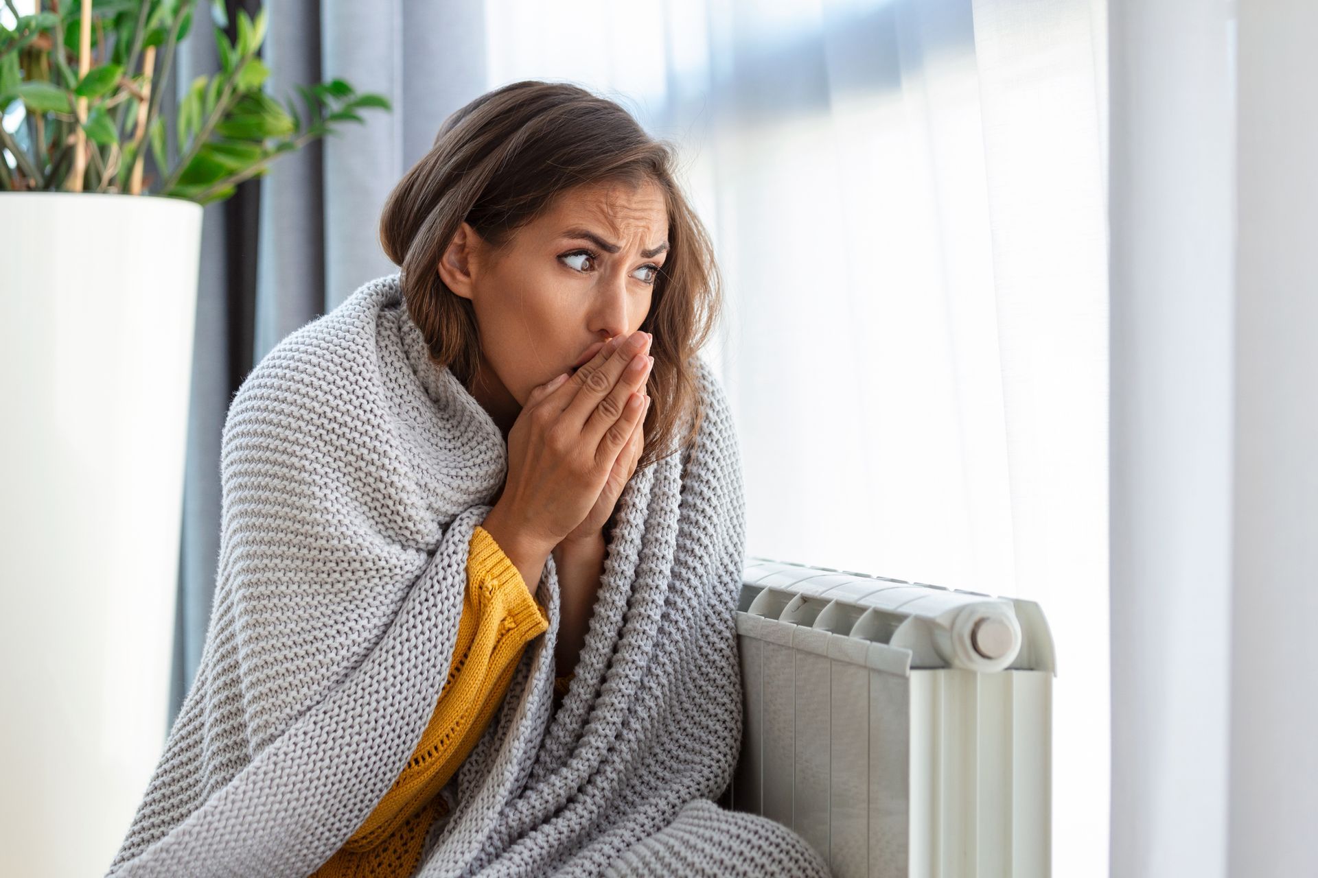 Woman freezing at home, sitting by the cold radiator.