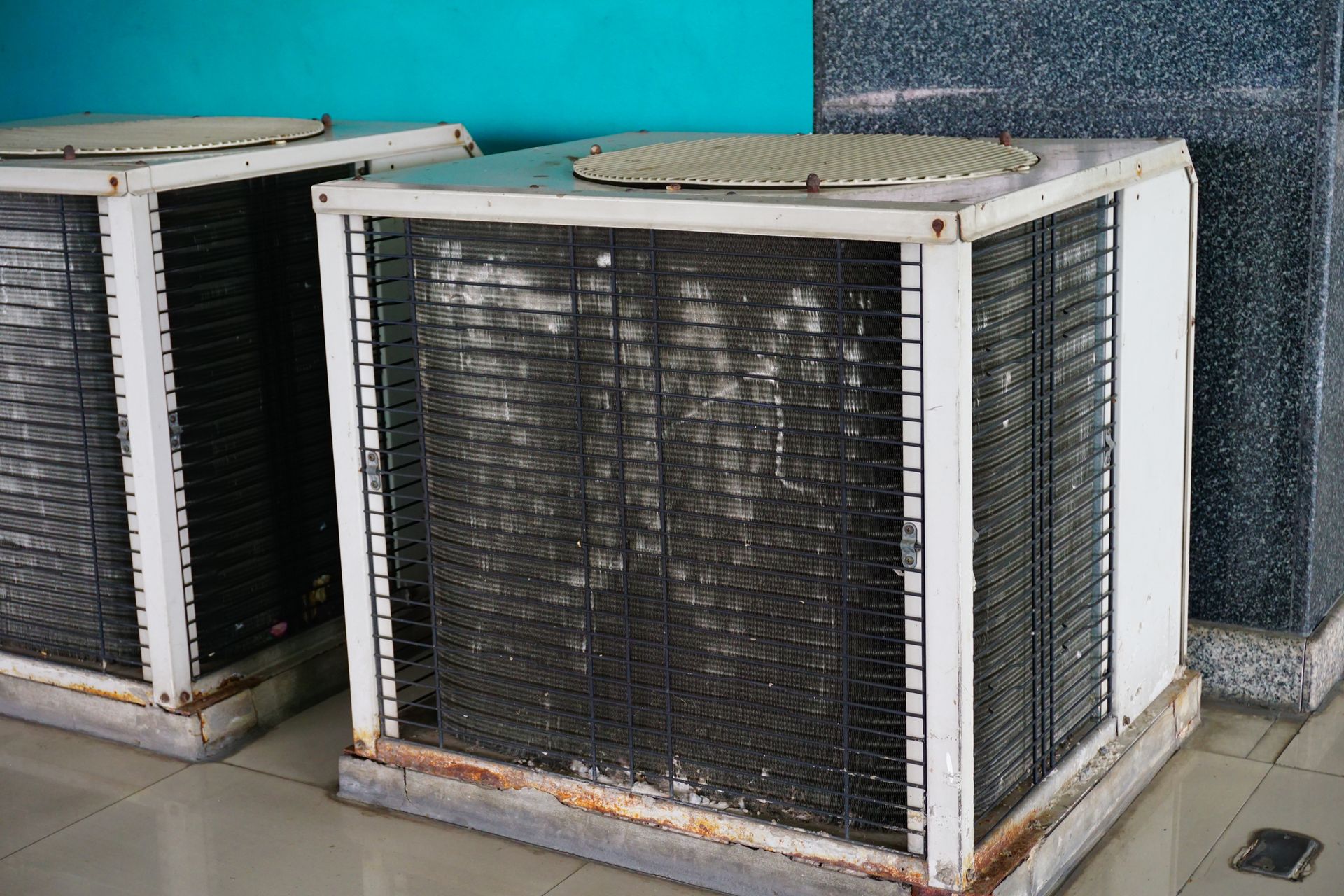 Two old air conditioners are sitting next to each other on the floor.