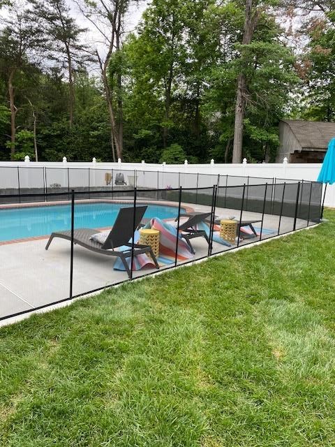 A swimming pool with lounge chairs and colorful towels surrounded by a black mesh safety fence in a backyard.