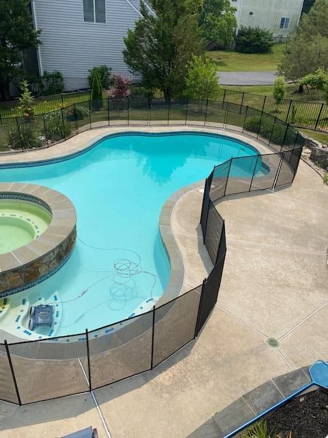 An elevated view of a turquoise-colored swimming pool with a hot tub and a black safety fence enclosure on a patio.