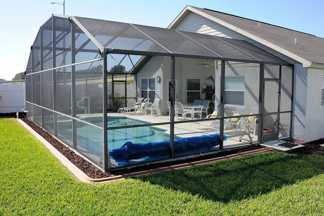 A screened-in patio and pool enclosure attached to the back of a house, surrounded by a lawn.