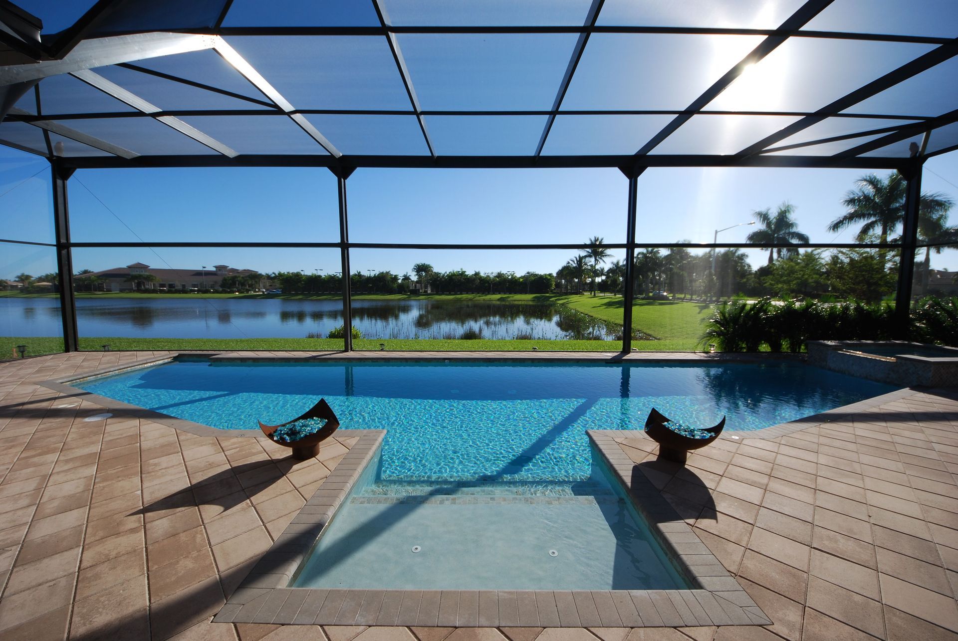 A screen-enclosed pool and spa overlooking a lake on a sunny day.
