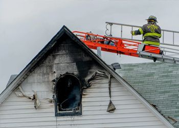 A fireman is standing on top of a ladder on the roof of a house.