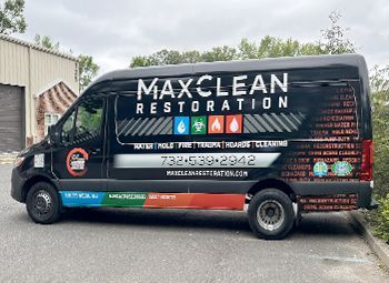 A black van with the word maxclean restoration on it is parked in front of a building.