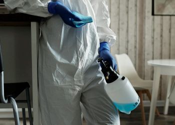 A person in a protective suit is cleaning a room with a spray bottle.