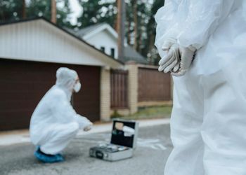 A couple of people in protective suits are standing in front of a house.