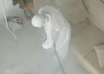 A person in a white suit is cleaning a room with a vacuum cleaner.