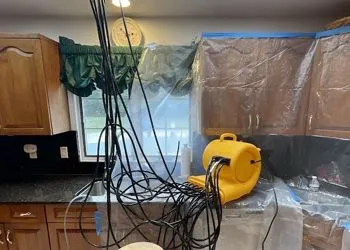 Kitchen with wires, a fan, and plastic sheeting covering cabinets.  Work in progress, likely water damage repair.