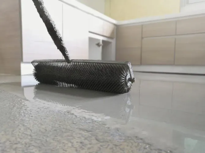 Using a spiked roller to remove bubbles from a fresh epoxy floor coating.