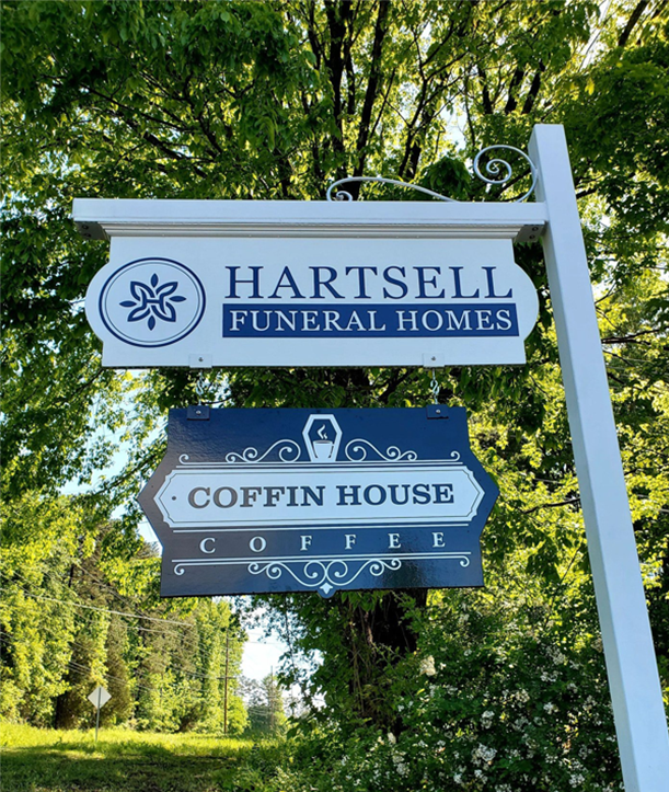 A sign for hartsell funeral homes is hanging from a pole in the grass.