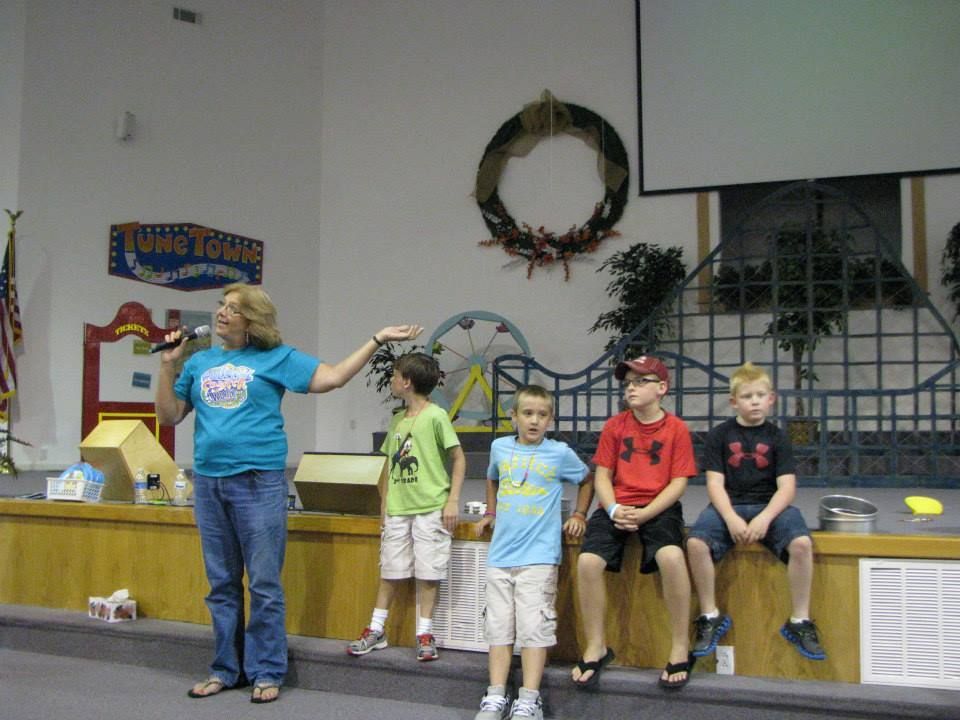 A woman is speaking into a microphone in front of a group of children