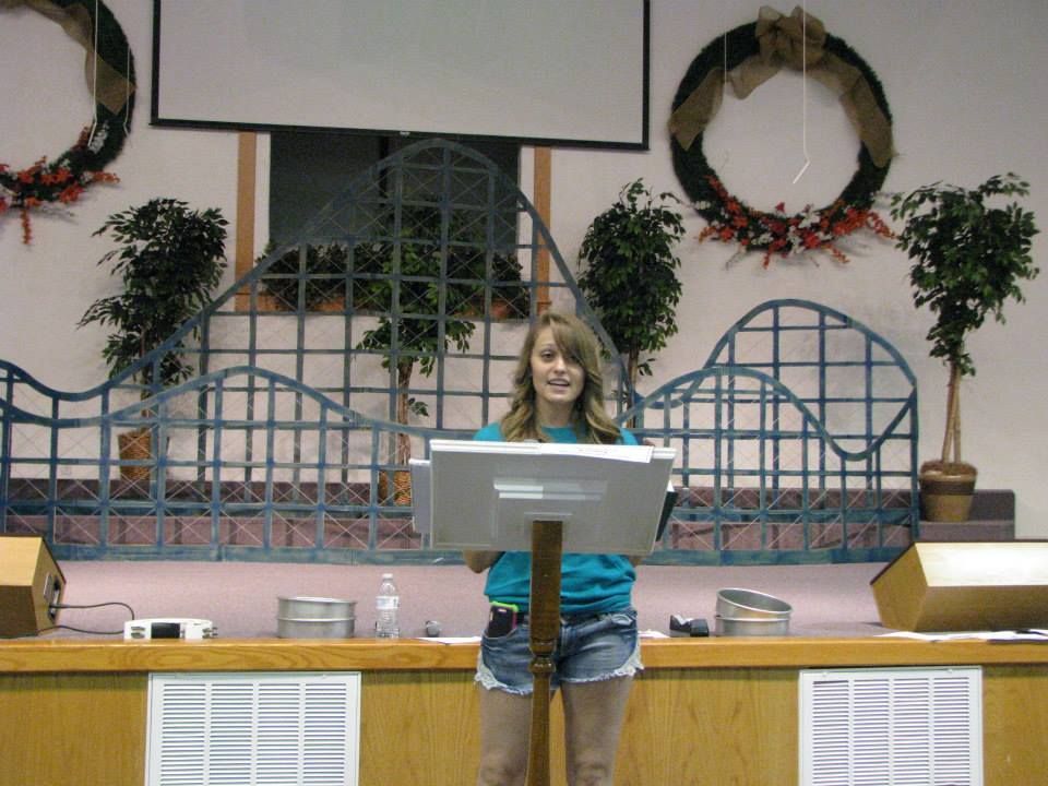 A woman stands behind a podium holding a computer monitor