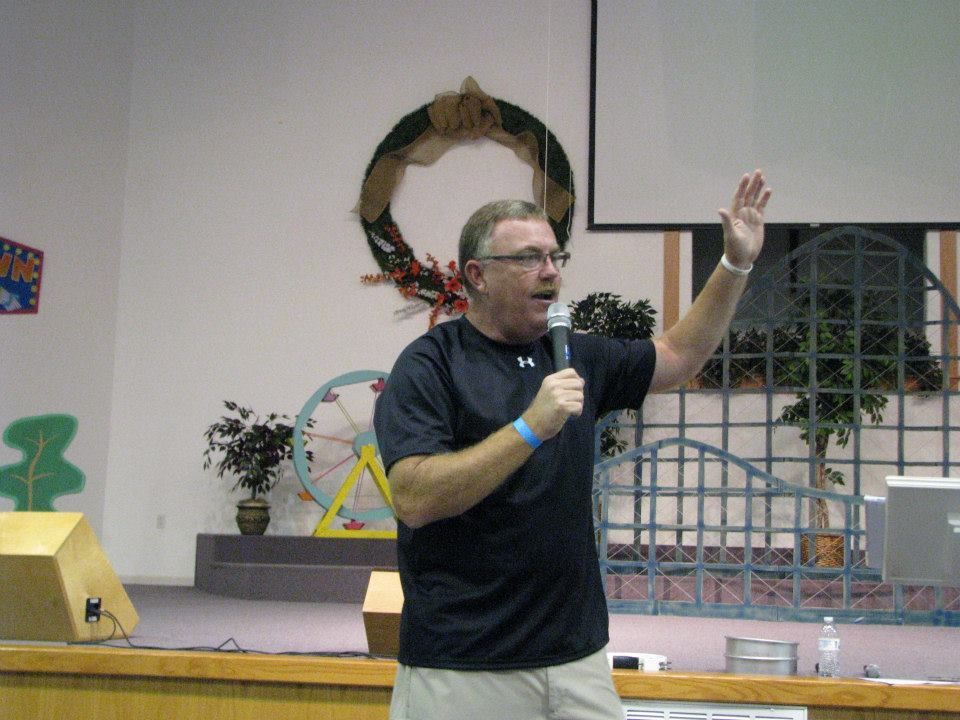A man in a black under armour shirt is speaking into a microphone