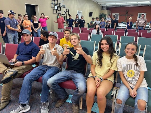 A woman is speaking into a microphone in front of a group of children