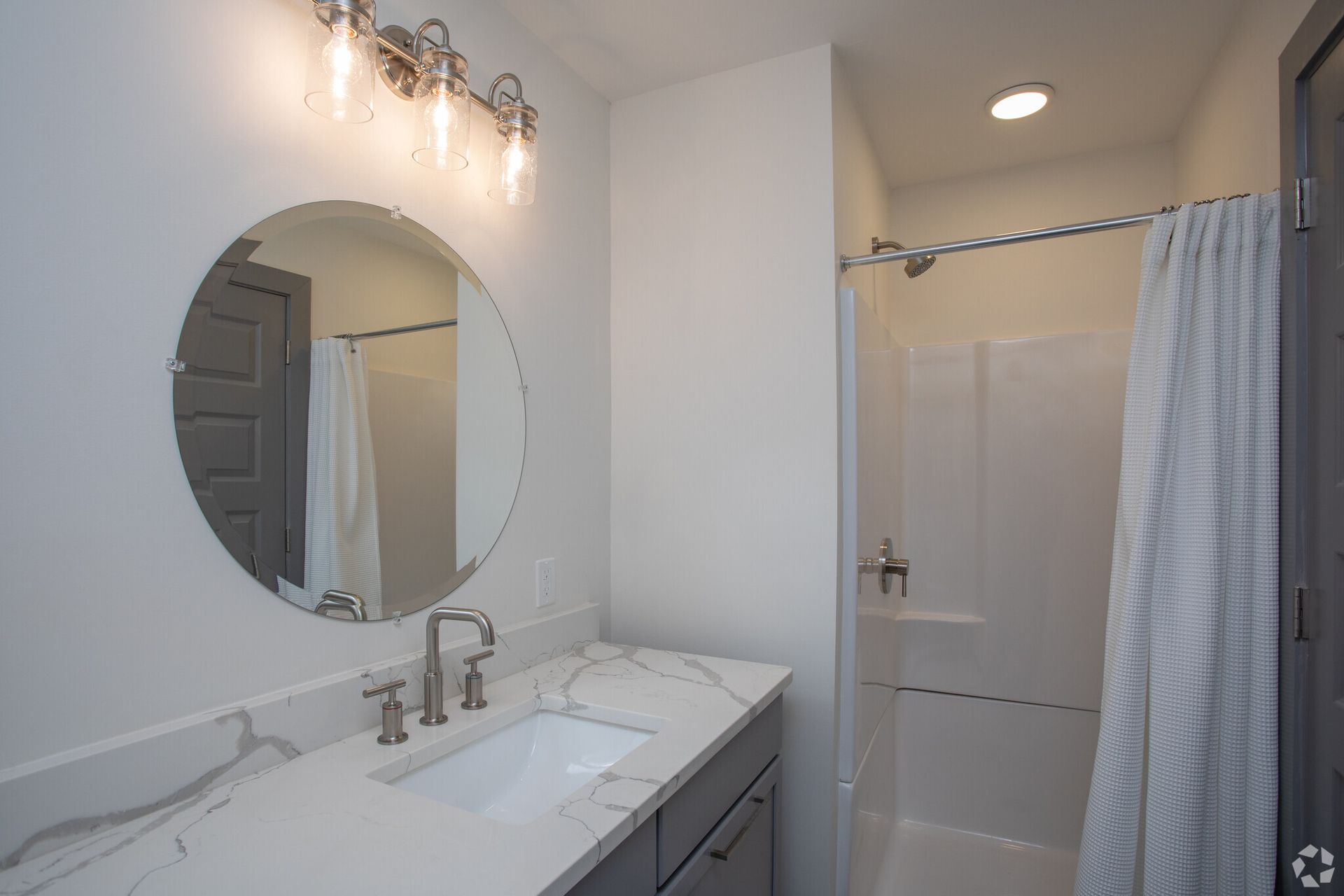 A bathroom with a sink, mirror and shower.