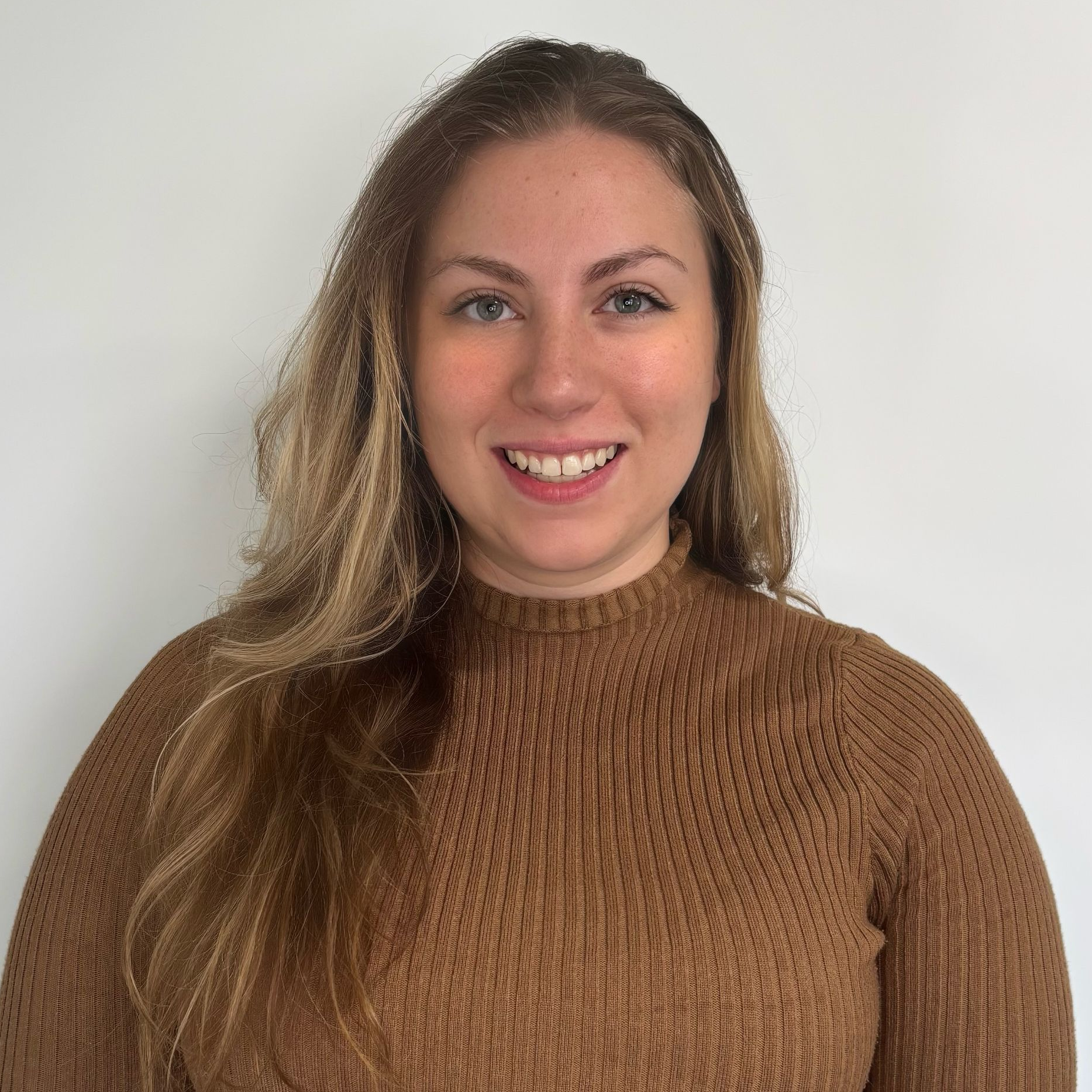 A woman wearing a purple sweater and a white shirt is smiling for the camera.