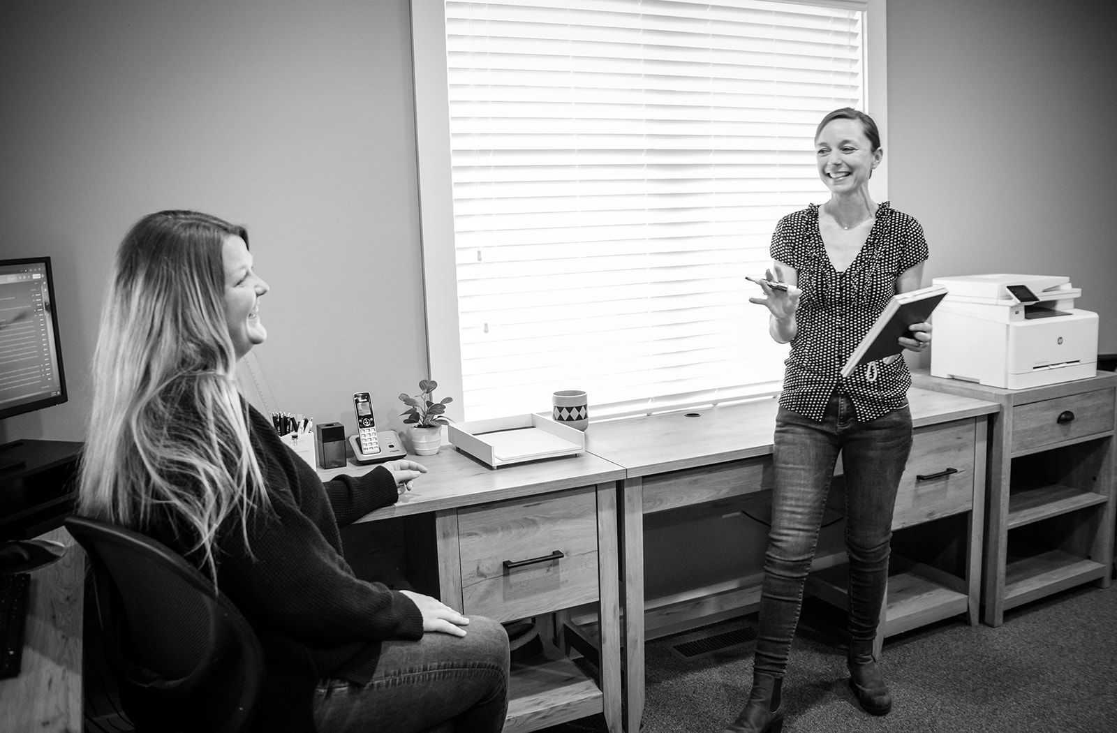 Two women are standing next to each other in a room in front of a window.