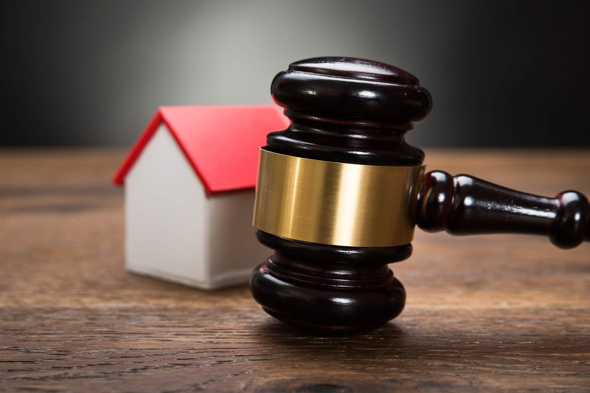  Gavel next to small house model on wooden table, symbolizing real estate law and auctions.