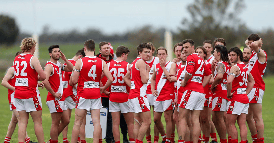A group of soccer players are standing in a huddle on a field.