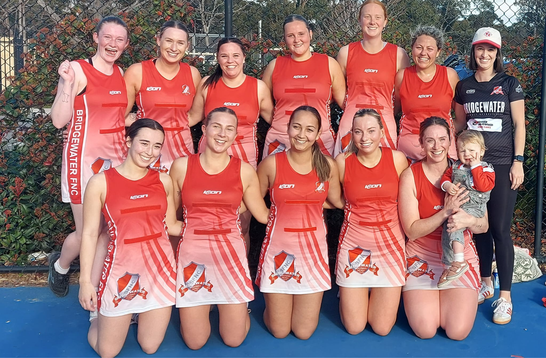 A netball team is posing for a picture on a blue court.