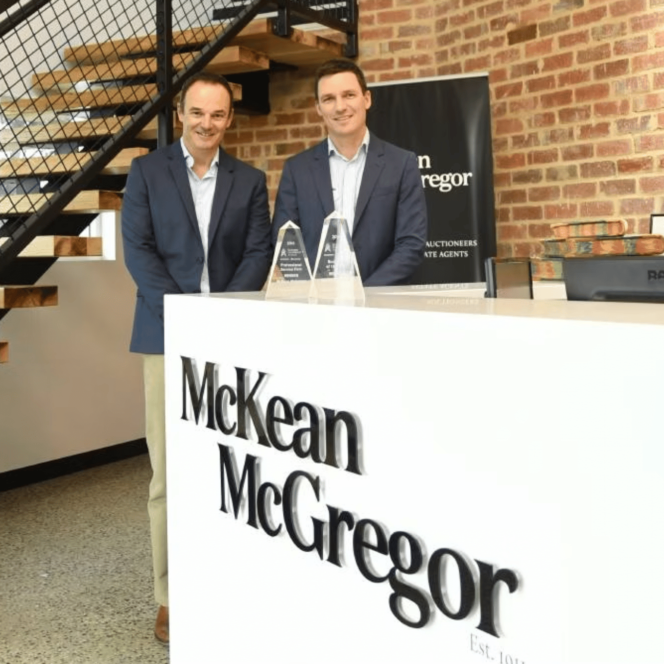 Two men standing in front of a mckean mcgregor sign