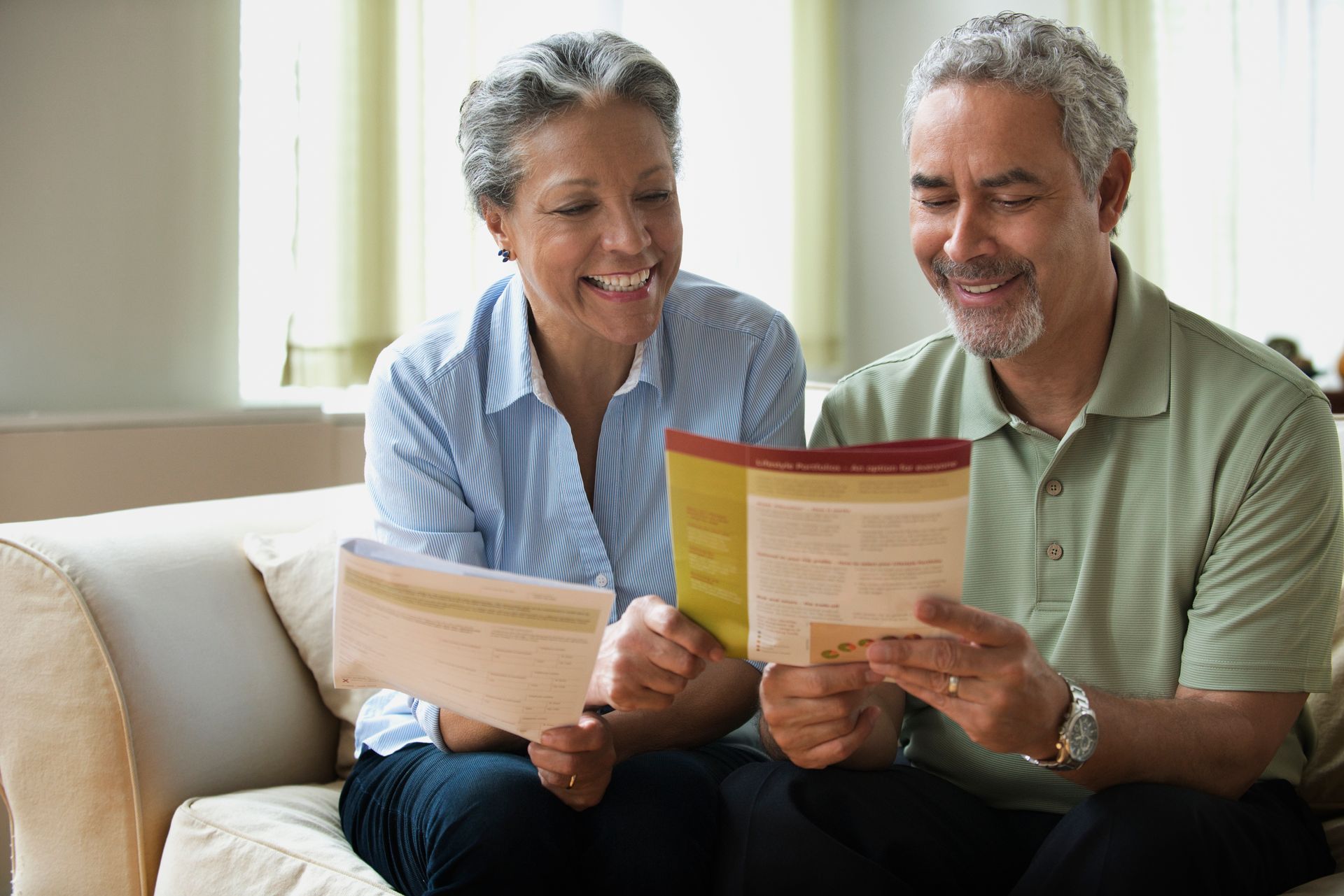 A couple reading a life insurance pamphlet on their sofa.